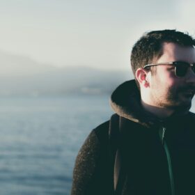 man wearing eyeglasses standing near body of water